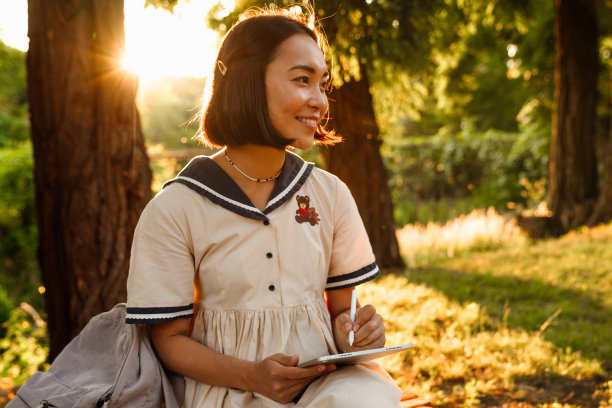 快乐的亚洲妇女在公园里坐着用触控笔在数字平板上画画图片下载