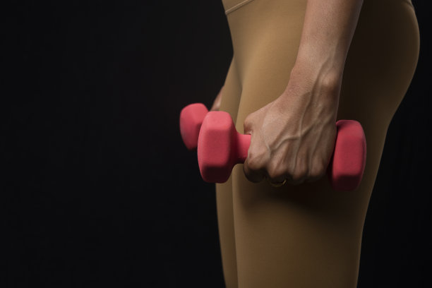 健身模特穿着紧身裤抱着哑铃站在工作室拍摄图片下载