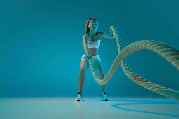 年轻的运动女孩训练与运动设备，绳索孤立在霓虹灯蓝色工作室背景。全身锻炼图片下载