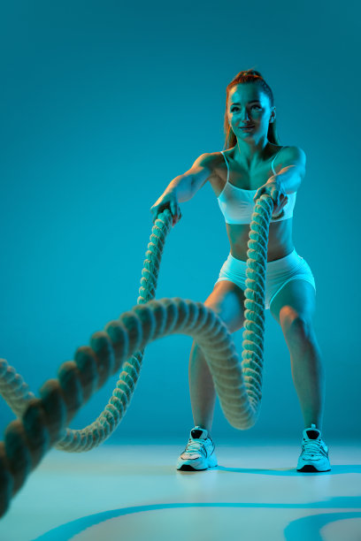 年轻的运动女孩训练与运动设备，绳索孤立在霓虹灯蓝色工作室背景。强度图片下载