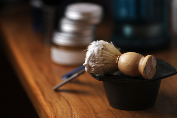 一套剃须设备和男士化妆品在木桌上，理发店。剃须概念与直剃刀，剃须刷和泡沫。男性胡须护理产品背景。图片下载