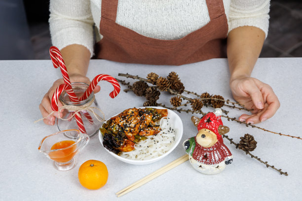 穿棕色围裙的女孩。配上米粉和鸡肉。节日装饰。深色的家庭厨房背景。圣诞节的概念图片下载