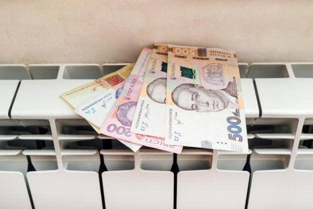 暖气散热器电池上的乌克兰格里夫纳钞票。冬季寒冷季节昂贵的供暖成本和不断上涨的能源账单价格。图片下载