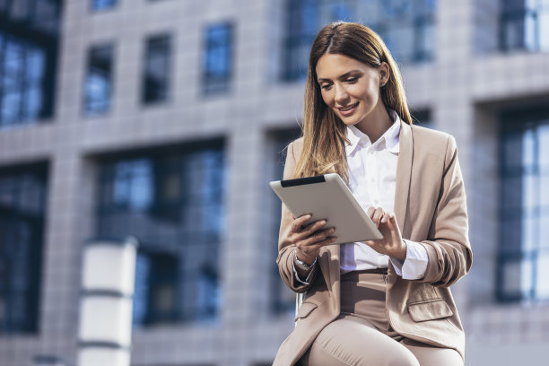 迷人的女商人使用一个数字平板电脑，而坐在前面的商业大楼。图片下载
