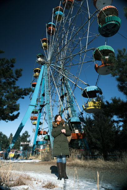 一名成年女子在冬季公园散步时，正看着一座古老的摩天轮图片下载