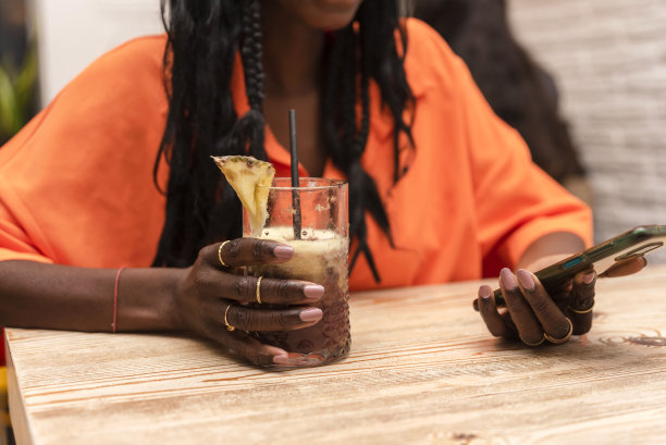一名不知名的非洲裔美国妇女一边拿着饮料一边用手机图片下载