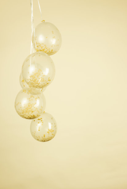 一个单色的黄色和金色的彩色透明气球对淡奶油黄色的背景图片下载