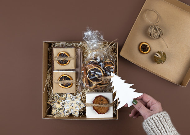 一个穿着羊毛衫的女人的手把礼物放在一个手工盒子里。橙子干，含天然精油的手工肥皂，木制圣诞玩具。概念公司或个人的礼物。图片下载