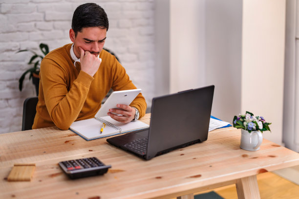 在新冠肺炎疫情期间，一位英俊的年轻人正在用平板电脑在家庭办公室工作。图片下载