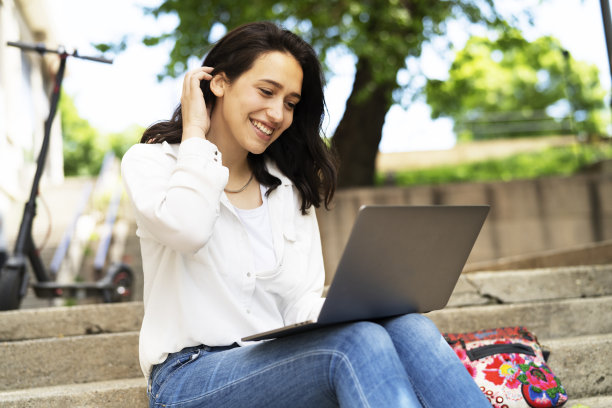 年轻的女商人坐在户外的台阶上，用笔记本电脑工作。图片下载