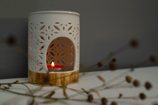 靠着灰色墙壁的桌子上放着一盏香薰灯，这是一个装有芳香油的烛台，上面点着蜡烛。极简主义的干花枝图片下载