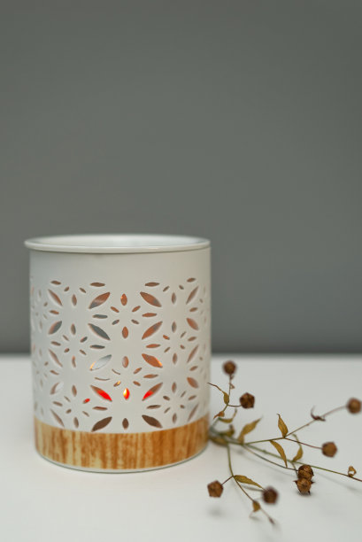 靠着灰色墙壁的桌子上放着一盏香薰灯，这是一个装有芳香油的烛台，上面点着蜡烛。极简主义的干花枝图片下载