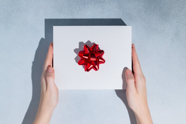 女性手握白色礼盒，蓝色背景上有红色蝴蝶结。复制设计空间。图片下载