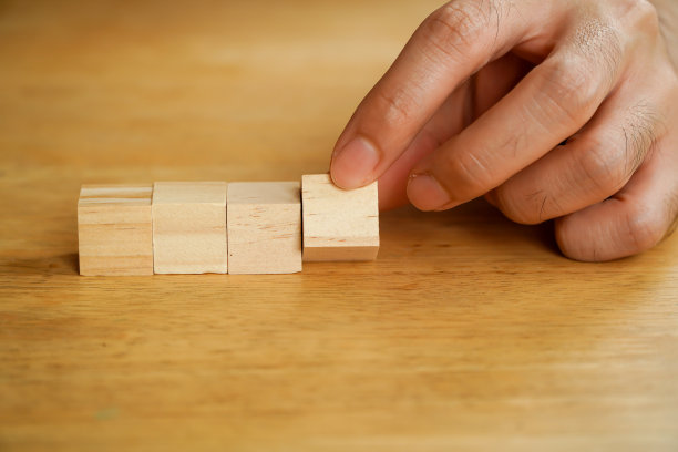 商人手里拿着两块木块排成一排，手把堆叠的木块排列成台阶放在木桌上图片下载