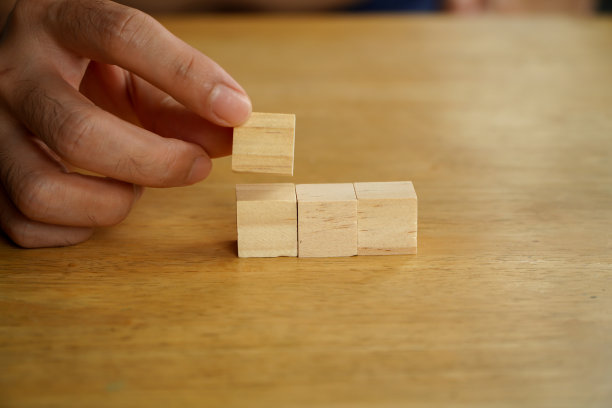 商人手里拿着两块木块排成一排，手把堆叠的木块排列成台阶放在木桌上图片下载