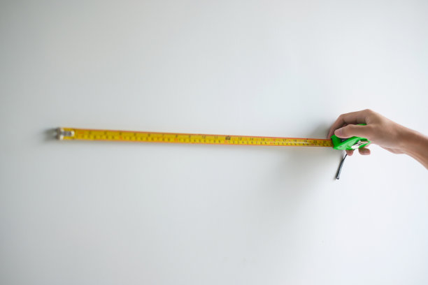 男人用卷尺测量家里的墙壁背景。DIY，室内设计，维修和改善家庭或公寓概念图片下载