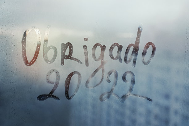 在葡萄牙语中，Obrigado的字母在英语中是再见，数字是2022，用手指把水涂在雨溅到日落窗户上的雾蒙蒙的玻璃上图片下载
