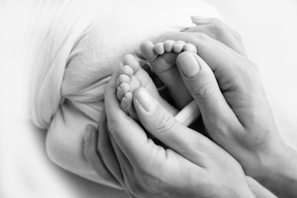 新生儿的腿，脚趾，脚和脚跟。用父母的手，爸爸，妈妈温柔地抱着孩子的腿。微距摄影，特写。黑白照片。高质量照片图片下载