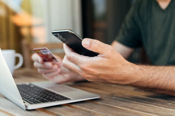 网上购物从家里阳台，男子使用笔记本电脑，移动智能手机和信用卡购买图片下载