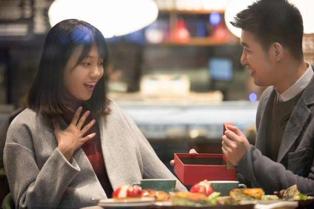 冬天，一对年轻的东亚夫妇坐在一家餐馆里，男人给了女人一份礼物——库存照片图片下载