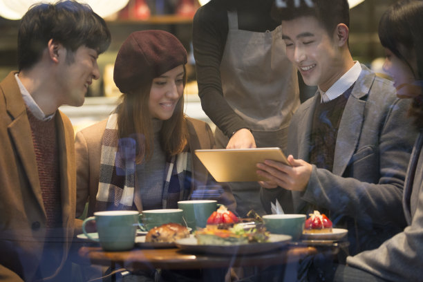 冬日里，两对年轻的东亚夫妇坐在咖啡馆里聊天，用的是订餐平板电脑上的照片图片下载