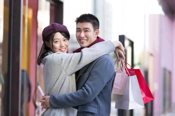 年轻的东亚夫妇在冬季繁忙的户外购物街上拥抱-库存照片图片下载