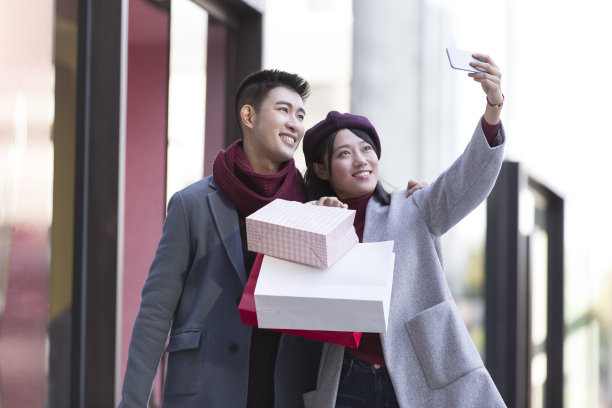 冬天，年轻的东亚夫妇在繁忙的户外购物街购物，用智能手机自拍图片下载