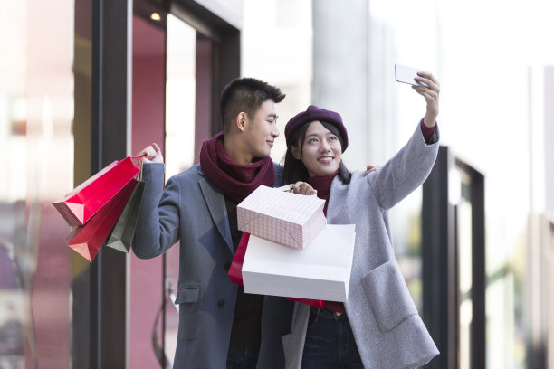 冬天，年轻的东亚夫妇在繁忙的户外购物街购物，用智能手机自拍图片下载