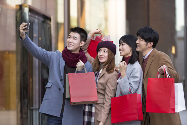 年轻的东亚夫妇在冬季繁忙的户外购物街购物时自拍-库存照片图片下载