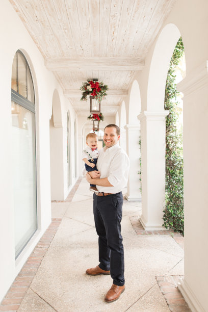 2022年12月，在南佛罗里达州，一位31岁的美国父亲和他10个月大的儿子穿着喜庆的红色圣诞服装拍摄家庭圣诞照片图片下载