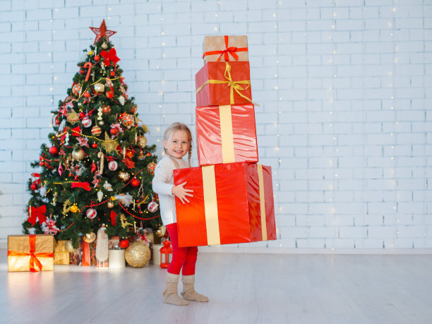 一个小女孩在白色的砖墙背景上有很多礼物。图片下载