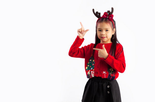 小亚洲孩子在红色运动衫圣诞主题服装摆手指指向空白的白色背景。图片下载