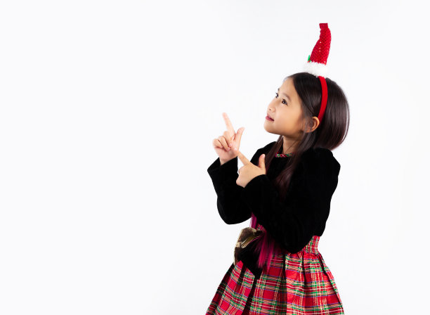 漂亮的亚洲孩子在圣诞主题服装手指指向白色背景。圣诞快乐。图片下载