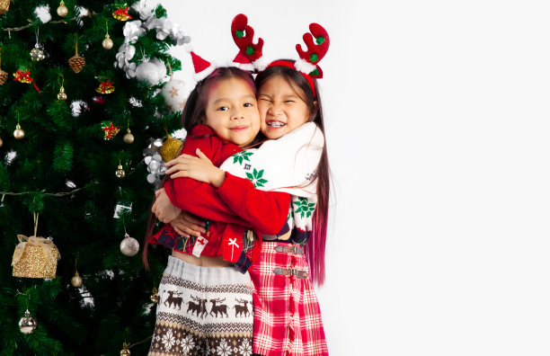 可爱的两个亚洲孩子女孩在圣诞主题服装戴驯鹿角头带摆拥抱在一起白色背景。图片下载