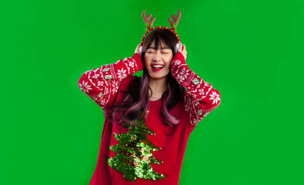 亚洲女人长发穿着红色毛衣快乐的脸听音乐在绿色屏幕背景。圣诞快乐的概念。图片下载