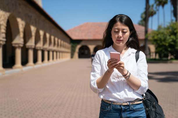 asian taiwanese woman international student reading course information on the phone near school Memorial Church on campus while sheâs on American study tour in California图片下载