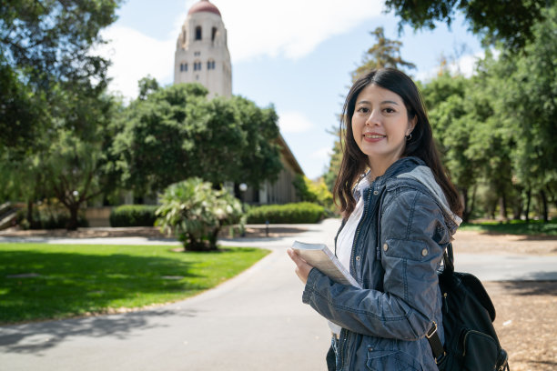 在美国加州，以学校校园和胡佛塔为背景，欢快的亚裔韩国女留学生拿着书，微笑着看着相机图片下载