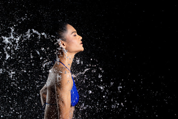 晒黑皮肤的亚洲妇女在比基尼pose在水工作室。水滴溅到身体上。有趣的情感女女孩对水攻击飘动和定格定格拍摄，黑色背景隔离图片下载