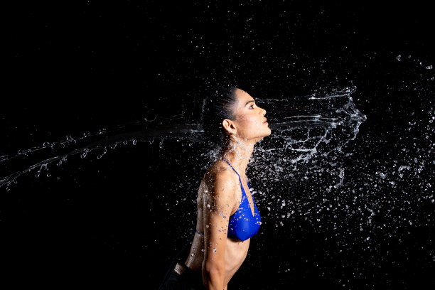 晒黑皮肤的亚洲妇女在比基尼pose在水工作室。水滴溅到身体上。有趣的情感女女孩对水攻击飘动和定格定格拍摄，黑色背景隔离图片下载