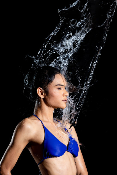 晒黑皮肤的亚洲妇女在比基尼pose在水工作室。水滴溅到身体上。有趣的情感女女孩对水攻击飘动和定格定格拍摄，黑色背景隔离图片下载