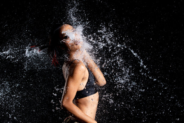 晒黑皮肤的亚洲妇女在比基尼pose在水工作室。水滴溅到身体上。有趣的情感女女孩对水攻击飘动和定格定格拍摄，黑色背景隔离图片下载