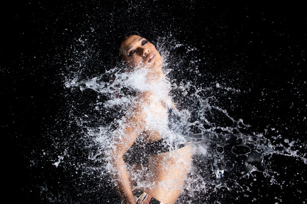 晒黑皮肤的亚洲妇女在比基尼pose在水工作室。水滴溅到身体上。有趣的情感女女孩对水攻击飘动和定格定格拍摄，黑色背景隔离图片下载