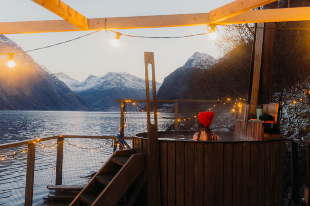 在挪威的冬季峡湾，一个戴着红帽子的女人在热水浴缸里放松的侧面视图图片下载