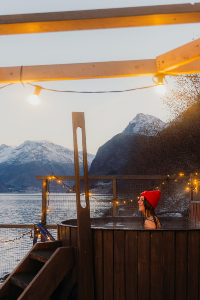 在挪威的冬季峡湾，一个戴着红帽子的女人在热水浴缸里放松的侧面视图图片下载