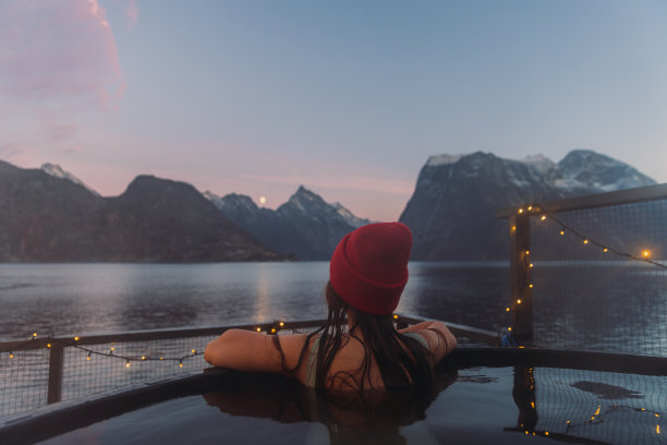 在挪威冬季峡湾的一个女人在热水浴缸放松的红帽子的后视图图片下载