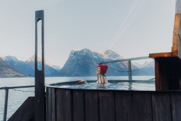 快乐的女人在红帽子放松在热水浴缸与挪威冬季峡湾风景的侧视图图片下载