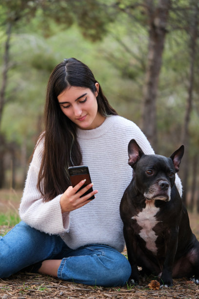 年轻的白人女人和她的狗坐在森林里打电话。图片下载