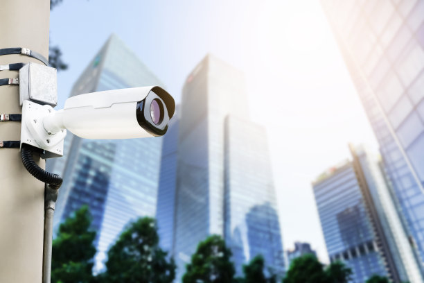 现代公共闭路电视摄像机在电杆模糊建筑背景。全天监控的录音摄像头。监视概念和带有复制空间的监视。图片下载