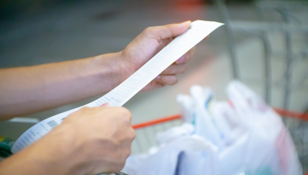 一名男子在超市或购物中心拿着一张很长的收据检查账单，手的焦点模糊。图片下载