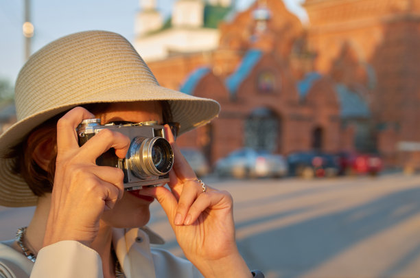一名女游客戴着草帽，拿着老式相机在街上拍照图片下载